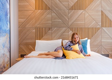 Smiling Woman In Bathrobe Relax On Bed At Modern Hotel Room. Female Traveler Relax In Luxury Hotel Room, Lying On White Bed Linen.