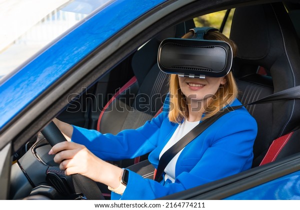 Smiling woman in the blue suit sitting in the car in VR\
goggles 
