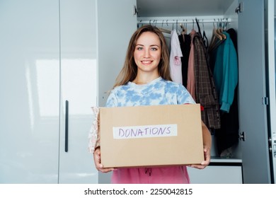 Smiling Woman with box of selected clothes from her wardrobe for donating to a Charity. Decluttering, Sorting clothes And Cleaning Up. Reuse, second-hand concept. Conscious consumer, sustainability. - Shutterstock ID 2250042815