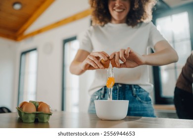 Smiling woman breaking open fresh eggs into white bowl, preparing ingredients for baking in modern kitchen, enjoying culinary hobby at home - Powered by Shutterstock