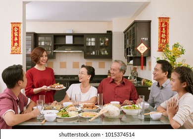Smiling woman bringing main dish to the Tet family dinner. Scrolls wishing luck and wealth in the background