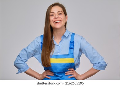 Smiling Woman Builder, Plumber Or Elictrician In Blue Overalls Keeps Her Hands On Hips. Isolated Portrait Of Happy Worker Girl With Long Hair.