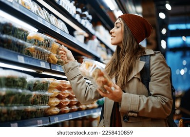 Smiling woman buying packed salad while shopping at grocery store. - Powered by Shutterstock