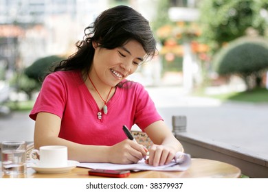 smiling woman at a cafe writing on a sheet of paper - Shutterstock ID 38379937