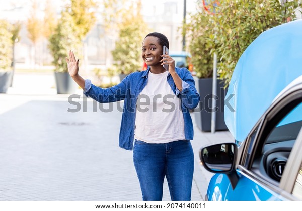 Smiling woman\
calling someone for help with his broken car. Young woman calling a\
car assistance service with her smartphone, her car has broken\
down. Woman calling car\
assistance