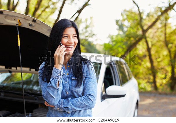 Smiling woman calling someone for help with his\
broken car