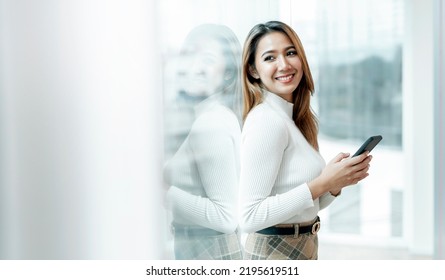 Smiling Woman In Casuals Standing In Office. Businesswoman With Mobile Phone In Hand Looking Away Outside.