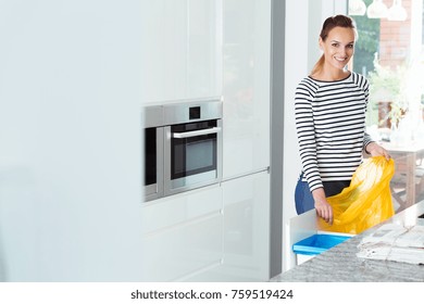 Smiling Woman Changing Garbage Bags In White Kitchen With Recycling Bins