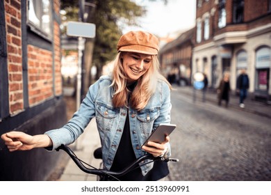 Smiling woman checking smartphone while holding bicycle on city street - Powered by Shutterstock