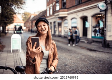 Smiling woman checking smartphone while holding bicycle on city street - Powered by Shutterstock