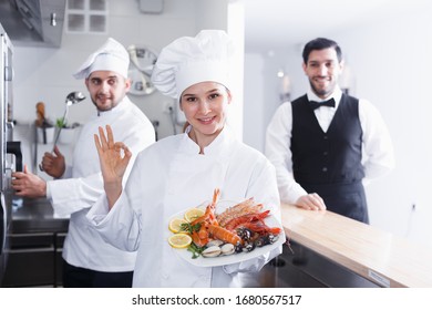 Smiling Woman Chef Approving Dish In Kitchen Of Fish Restaurant Before Serving Guests