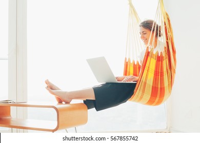 Smiling woman chilling in hammock with laptop. Freelancer and her workspace - Powered by Shutterstock