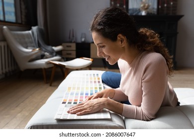 Smiling woman choosing color from samples catalogue, preparing for house renovation, sitting on couch, happy young female using palette of wall paint colors, interior designer working on project - Powered by Shutterstock