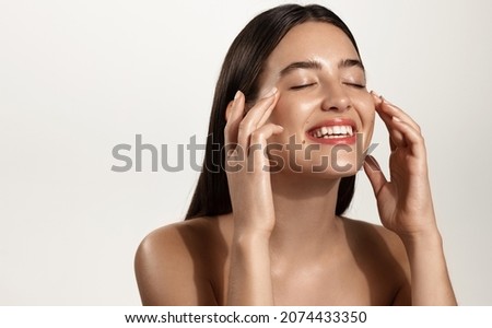 Smiling woman with clean glowing facial skin washing her face, rubbing in cream skincare product for anti-aging, lifting spa effect, standing over white background