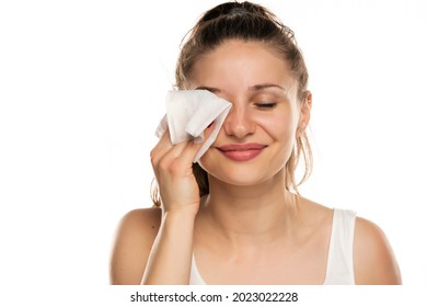 A smiling woman cleans makeup from her face with wet wipes on a white background - Shutterstock ID 2023022228