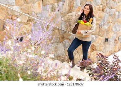 Smiling woman climbing stairs talking phone shopping bag groceries