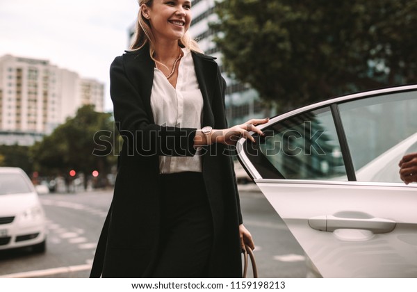 Smiling woman commuter getting out of a taxi.\
Businesswoman getting off a\
cab.