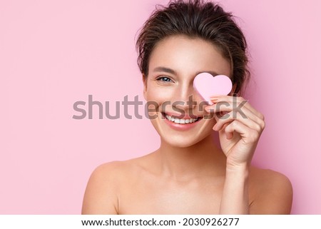 Smiling woman with cosmetic sponge covering one eye. Photo of woman with perfect makeup on pink background. Beauty concept