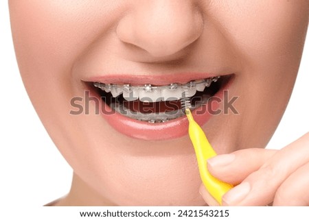 Smiling woman with dental braces cleaning teeth using interdental brush on white background, closeup