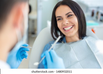 Smiling Woman In Dental Chair With Doctor Holding Dental Mirror