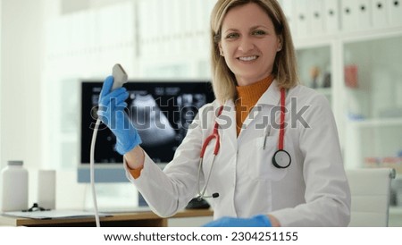 Smiling woman doctor holding ultrasound probe in hands to diagnose early pregnancy in clinic