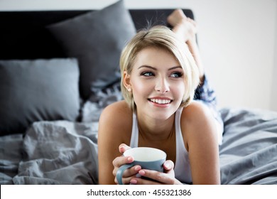 Smiling Woman Drinking A Coffee Lying In Bed At Home Or Hotel.