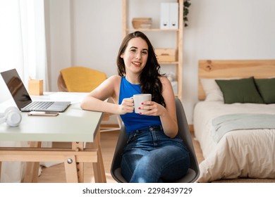 Smiling woman drinking coffee sitting at desk at home. - Powered by Shutterstock