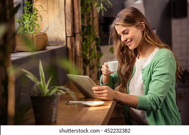 Smiling woman drinking coffee and using tablet in the cafe