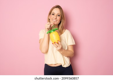 Smiling Woman Drinking Pinapple Juice Standing Isolated Over Pink Background.