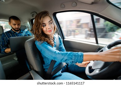 Smiling woman driving a car with male passenger using latop.