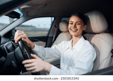 Smiling woman driving a car in a parking lot, hands on the steering wheel, joyful expression, safe driving, sunlight through windshield - Powered by Shutterstock