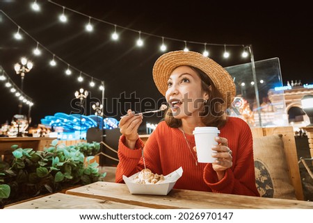 Smiling woman eats a sweet cake with ice cream and drinks coffee in a night cafe with lights