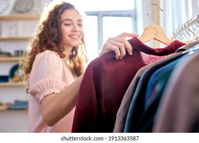 smiling woman in an ecological shop choosing between various clothes represented in eco shop, eco cotton and clothes from organic materials - Shutterstock ID 1913363587
