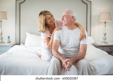 Smiling Woman Embracing Man On Bed In Bedroom