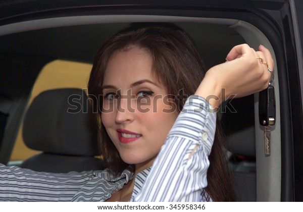 Smiling woman enjoying in a car and showing her new\
car keys.
