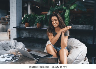 Smiling woman enjoying remote work break, sitting with laptop and tablet in cozy cafe corner decorated with green plants, showing happy freelance lifestyle - Powered by Shutterstock - Get 15% off with code: PIKWIZARD15