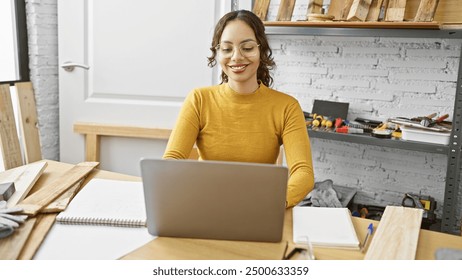 A smiling woman entrepreneur in a carpentry workshop with laptop, tools, and wood. - Powered by Shutterstock