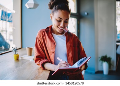 Smiling woman feeling good while planning organisation of knowledge event with colleagues in university campus, successful hipster girl notes interesting minds in textbook during free time on leisure