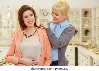 Smiling Woman Fitting Nacklace In Jewelry Store With The Help Of A Salesperson