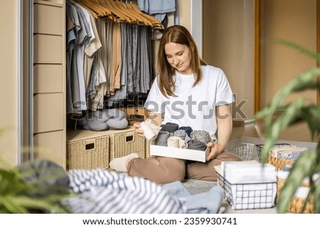 A smiling woman folds her clothes and puts them in metal and jute baskets. The concept of space organization and storage.