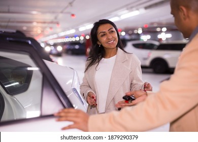 Smiling Woman Gets Into A Car In An Underground Parking Lot. Man Opens The Car Door