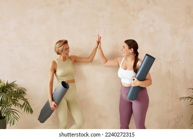 Smiling Woman Giving Five After Yoga. Female Friends Laughing And Holding Yoga Mats After Yoga Session Together At Home. Attractive Girls In Sportswear Spending Free Leisure Time - Powered by Shutterstock