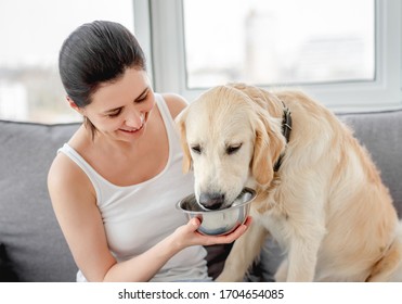 Smiling Woman Giving Water To Cute Dog At Home