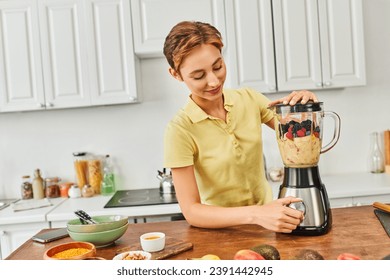 smiling woman grinding fresh fruits in blender while making delicious vegetarian smoothie in kitchen - Powered by Shutterstock