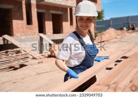 Smiling woman handyman helping to unload and sort wooden beams