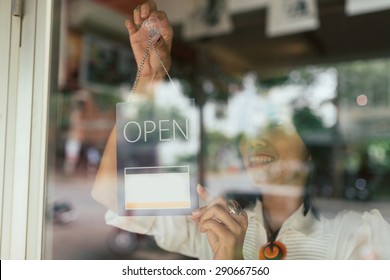 Smiling Woman Hanging Open Sign On The Glass Door