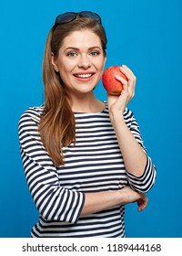 Smiling woman with healthy teeth holding red apple. Portrait on blue.