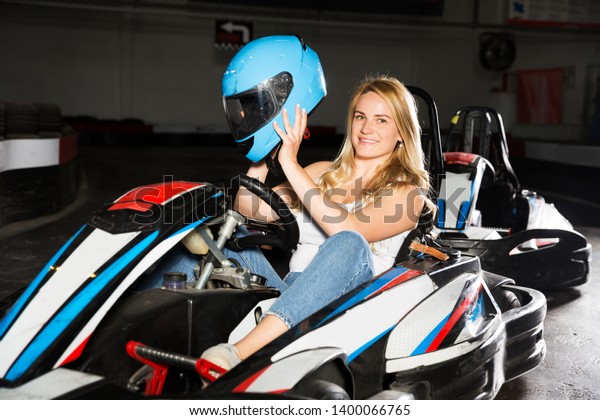 Smiling woman with helmet sitting in car for karting\
in sport club