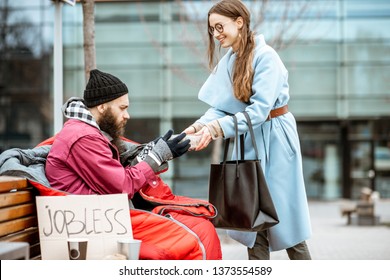 Smiling Woman Helping Homeless Beggar Giving Some Food Outdoors. Concept Of Helping Poor People