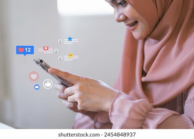 Smiling woman in hijab engaging with social media on smartphone.